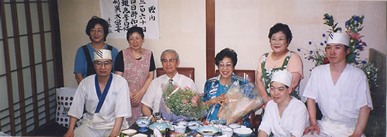 創業者　八木 敏夫（中央左）　妻　八木 トシ（中央右）〈創業者八木 敏夫の喜寿を祝う会にて従業員との集合写真〉